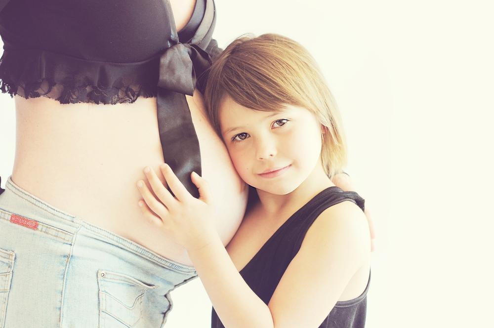 A young girl presses her ear to a woman's pregnant belly