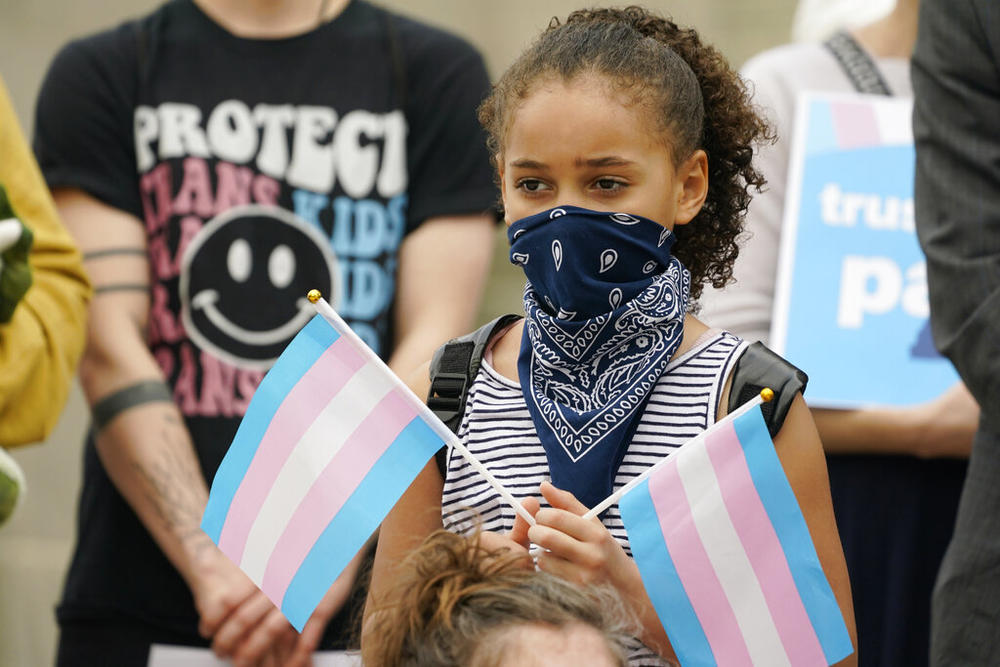 A young child holds a pair of trans pride flags at a noon gathering on the steps of the Mississippi Capitol in Jackson, as they protest House Bill 1125, which bans gender-affirming care for trans children, Wednesday, Feb. 15, 2023.