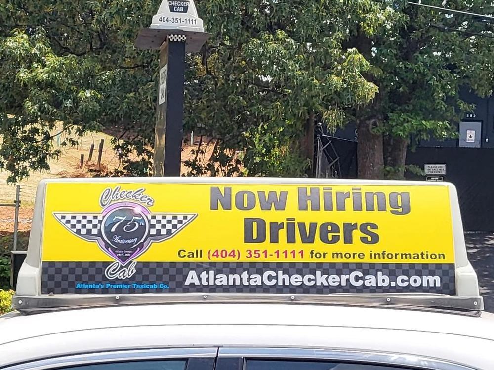 The sign on top of a yellow taxi cab is shown reading "Now Hiring Drivers."