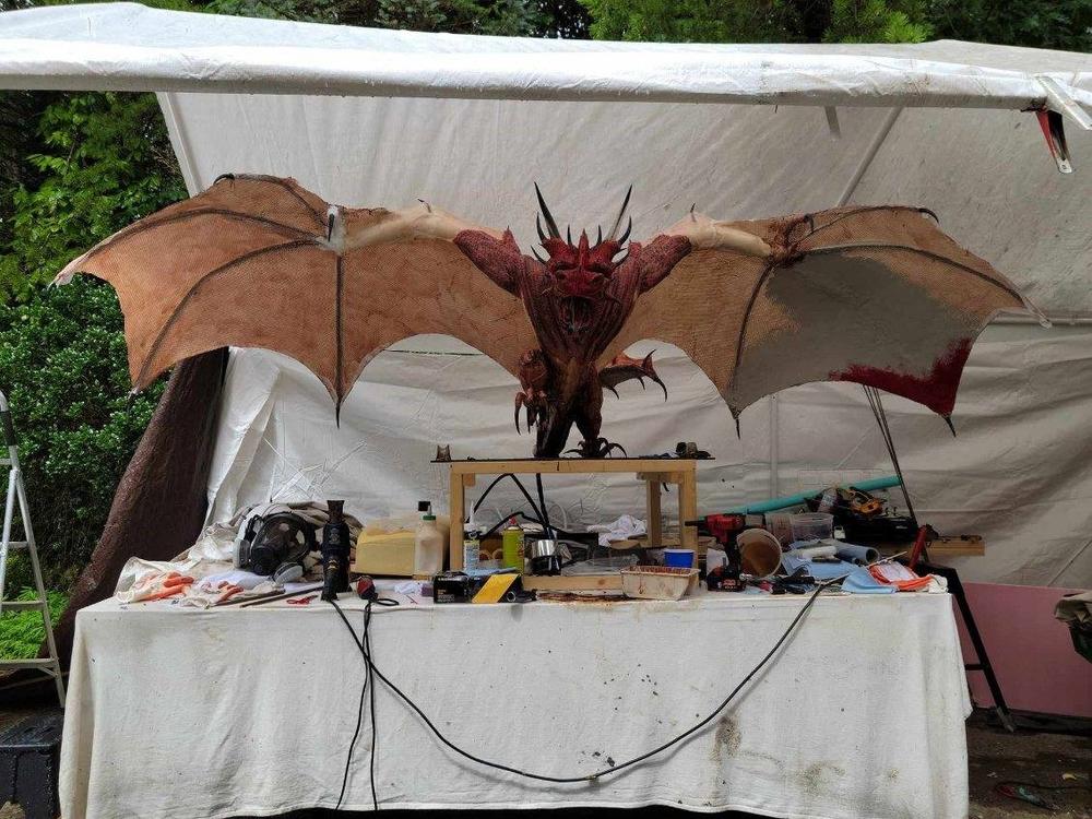 A mock-up of a horned, winged dragon sits on a work table with tools underneath a canopy.
