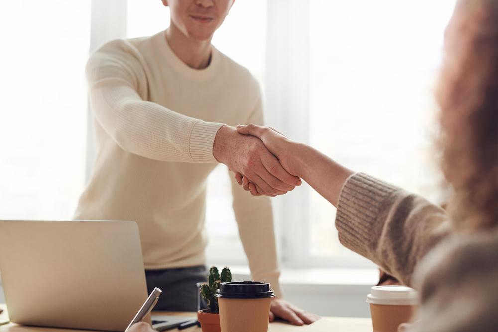 Stock photo of a man and woman shaking hands across a desk with a laptop