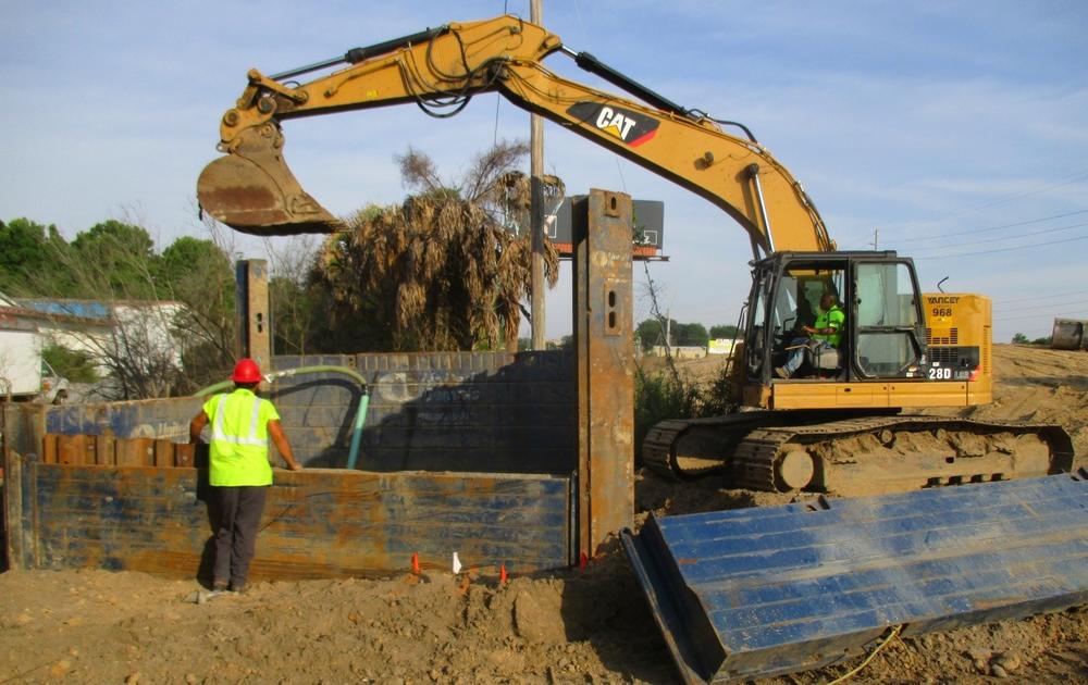 A backhoe is used at a construction site in Savannah, with a construction worker watching from a distance.