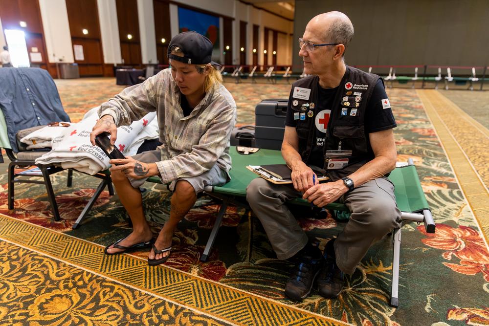A volunteer with the American Red Cross sits with Chris Phillips who evacuated Lahaina.