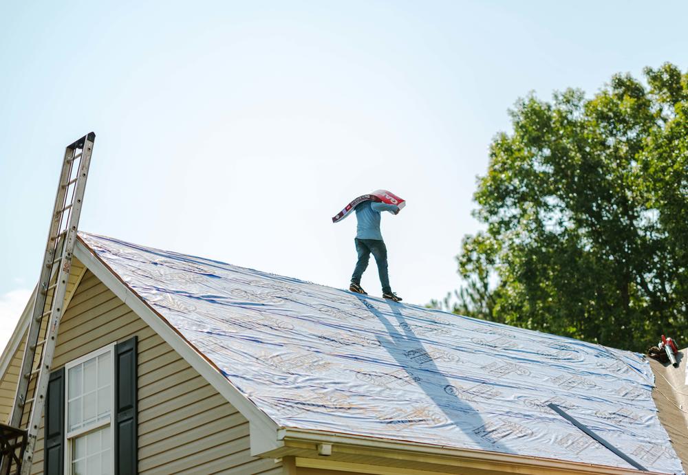 Roofer Rafael Romero carries a stack of shingles while walking down the spine of a roof in Gainesville.