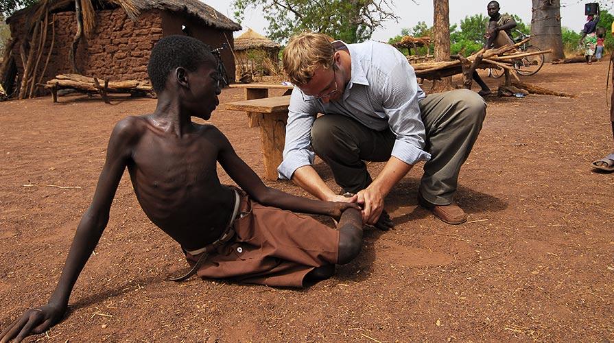 Adam Weiss examining a young Ghanian boy's leg for Guinea worms.