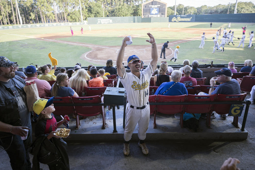 Savannah Bananas catcher Vinny Rauso, center, tries to get fans to cheer before throwing a free T-shirt to the loudest section, during the team's baseball game against the Florence Flamingos, June 7, 2022, in Savannah, Ga. A new exhibit dedicated to the sport's wackiest team, the Bananas, will open Friday at the Baseball Hall of Fame in Cooperstown, N.Y.