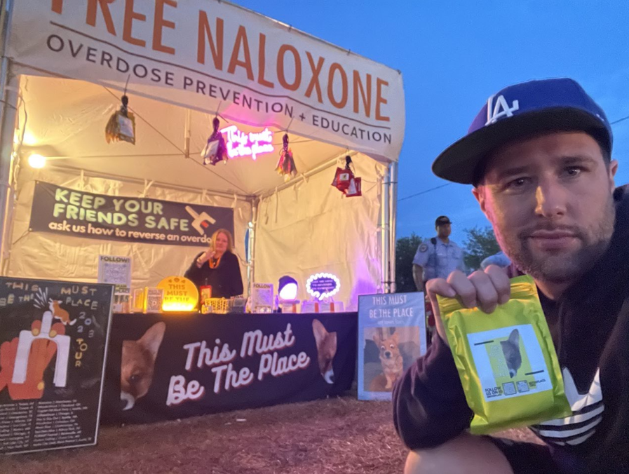 William Perry of This Must Be The Place holds a free overdose prevention kit outside a booth