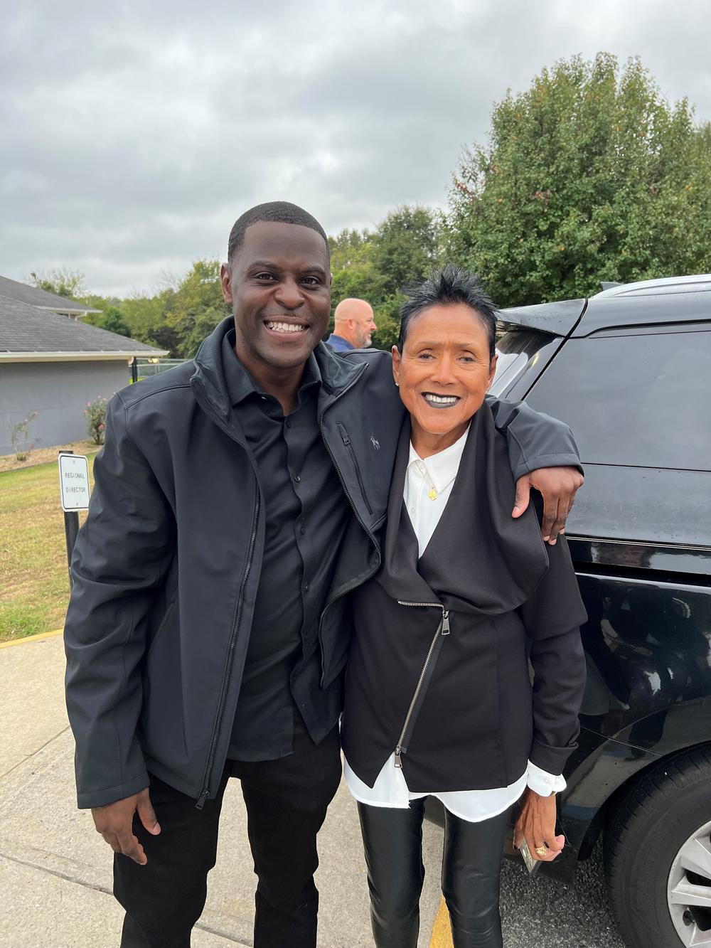 Michael Lewis is shown posing for a photo with Elaine Brown in this photo taken outdoors in front of a vehicle.