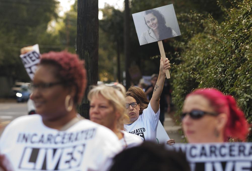 A protester carries a photo of Stephanie Widener who died of sepsis in Georgia Department of Corrections custody during a protest of prison conditions outside the Georgia Governor's Mansion on October 3, 2023.