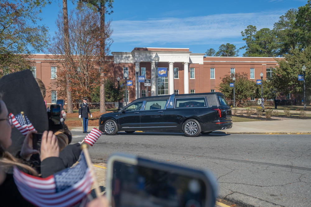 A hearse is shown on a road in front of a college building.