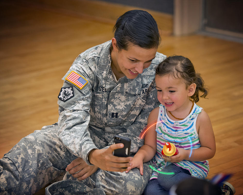 A military servicemember holds a cellphone up for a child