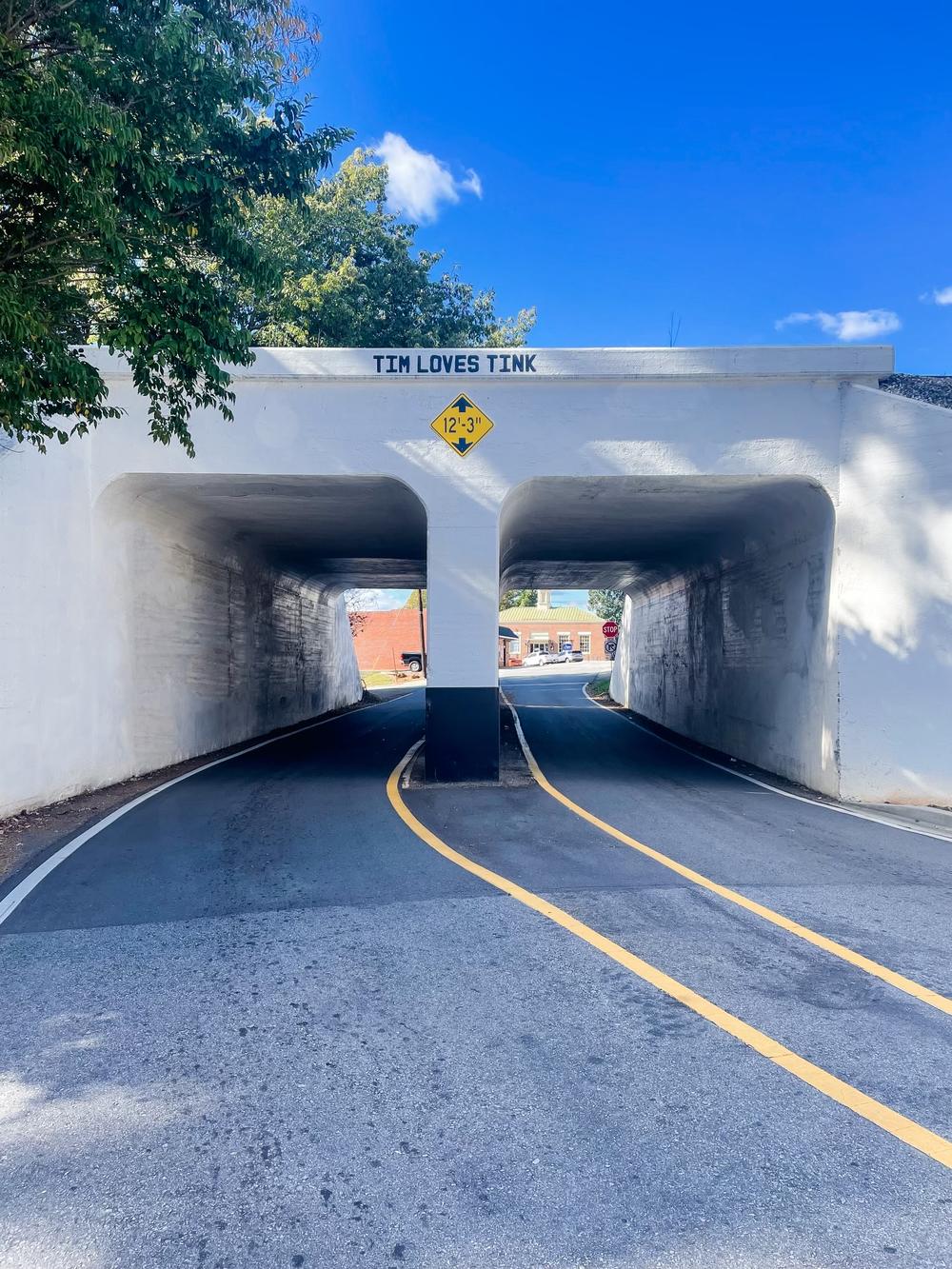 A highway underpass is shown. Stenciled on the underpass is a message: "Tim Loves Tink."
