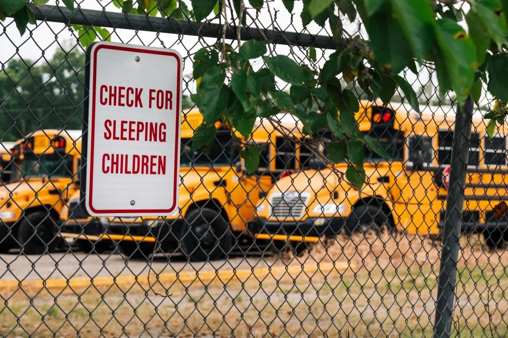 A sign reminding drivers to check for sleeping children hangs on the fence of a school bus parking lot. Credit:Justin Taylor/The Current