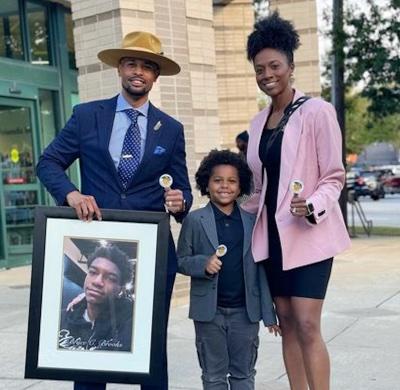 Alfred “Shivy” Brooks with son Christian and wife Crystal. Shivy holds a portrait of his son Bryce, who died last year saving young children from drowning.