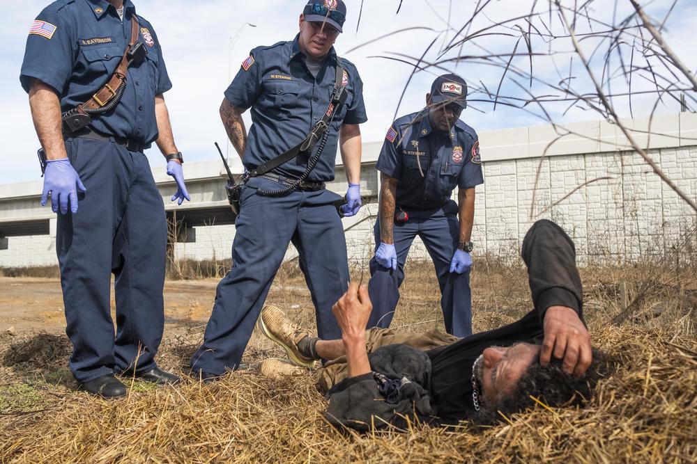Firefighters leading a contingent of homeless census takers tend to an unsheltered man experiencing a medical issue by Interstate 16 in Macon. Firefighters and other first responders who frequently encounter unsheltered people informed the direction and geography of Macon's 2024 census of the unsheltered. 