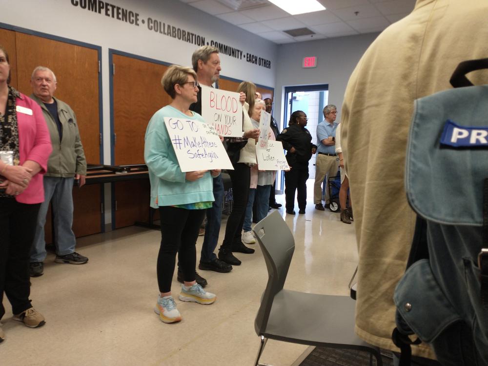 Several demonstrators are shown holding signs inside of an office building. One sign says "Blood on Your Hands."