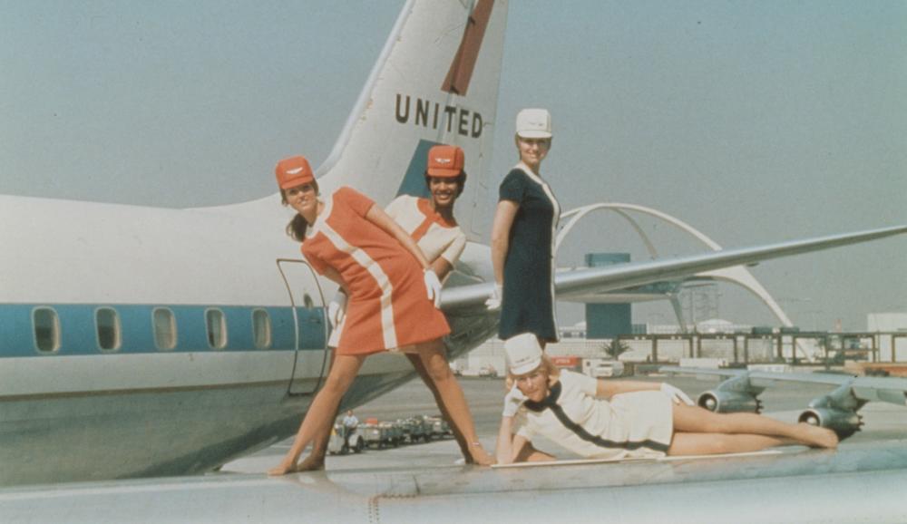 Four stewardesses posed on wing of airplane, circa 1965.