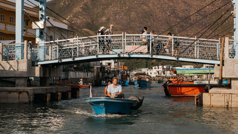 Chef Curtis Stone riding a small boat under a bridge in Hong Kong
