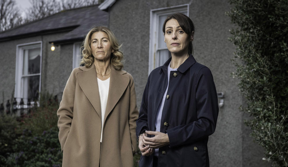 Two women in coats standing outside a house on a dark day.