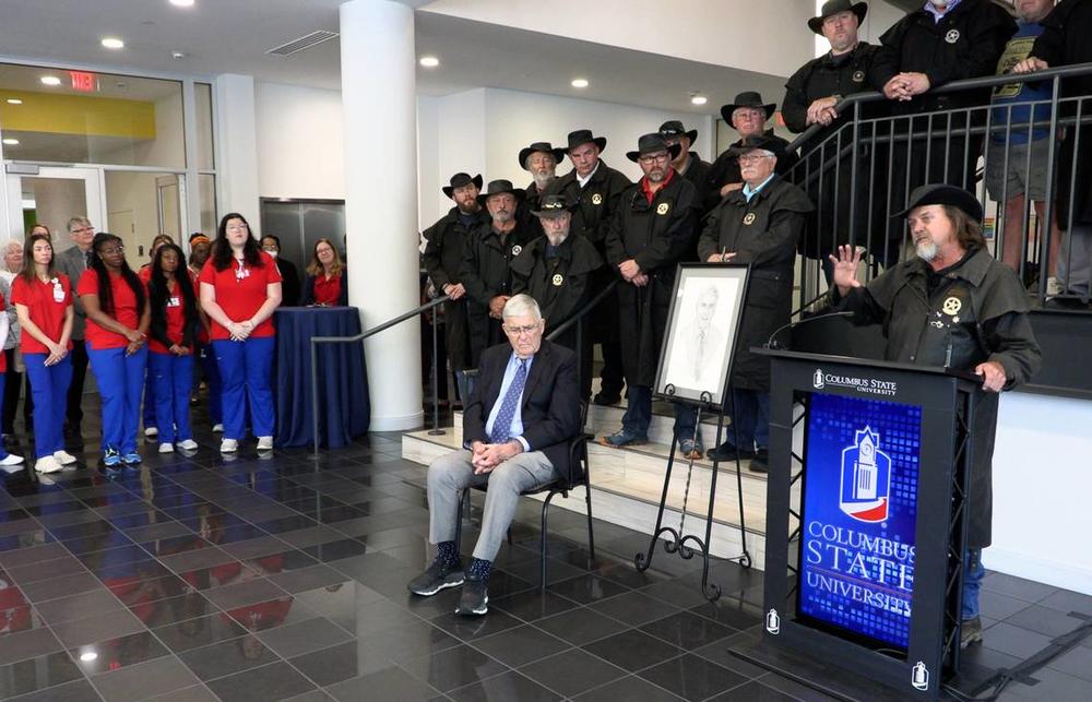 Scott Ressmeyer, co-owner of Country’s Barbecue and founder of the Miracle Ride, speaks Thursday afternoon during a celebration of the new mother-baby simulation lab at Columbus State University’s School of Nursing. The simulation has been named in honor of Dr. Cecil F. Whitaker, M.D., seated. Whitaker is a retired OB-GYN. 03/28/2024 Mike Haskey mhaskey@ledger-enquirer.com  