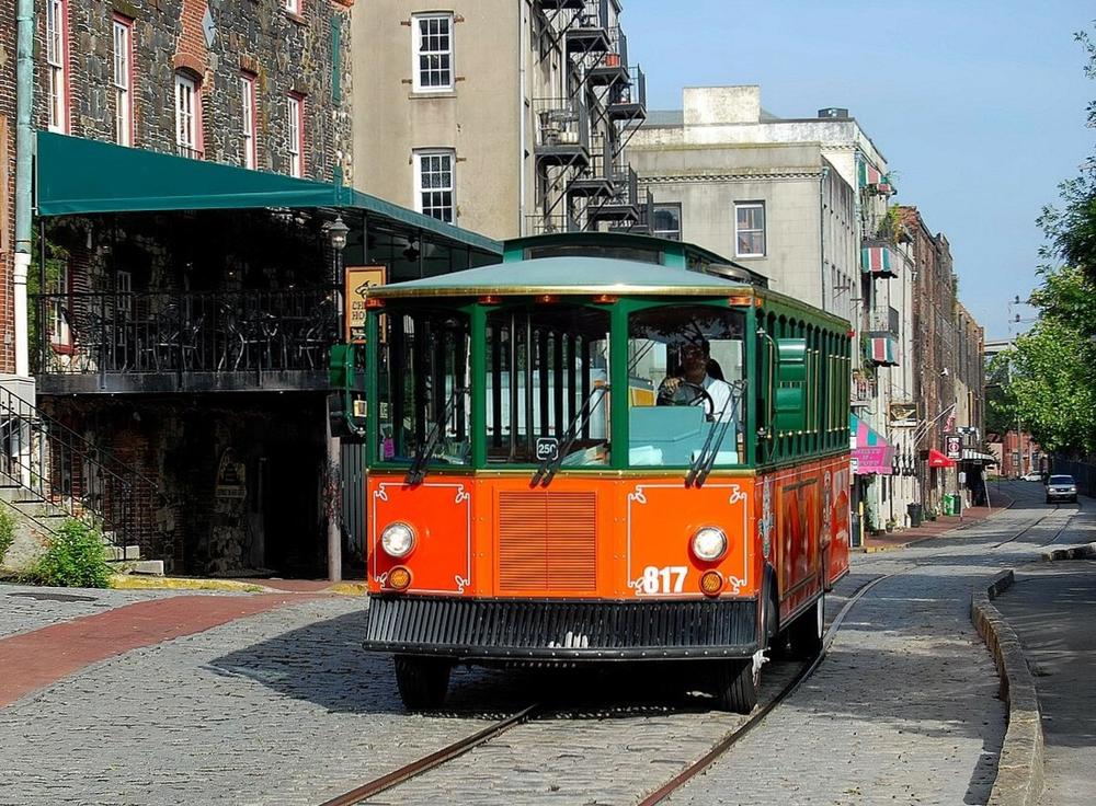 A trolley tour bus drives down River Street in downtown Savannah.