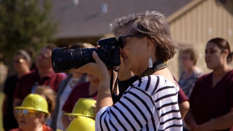 A woman standing outside preparing to take a photograph with a camera with a long lens.
