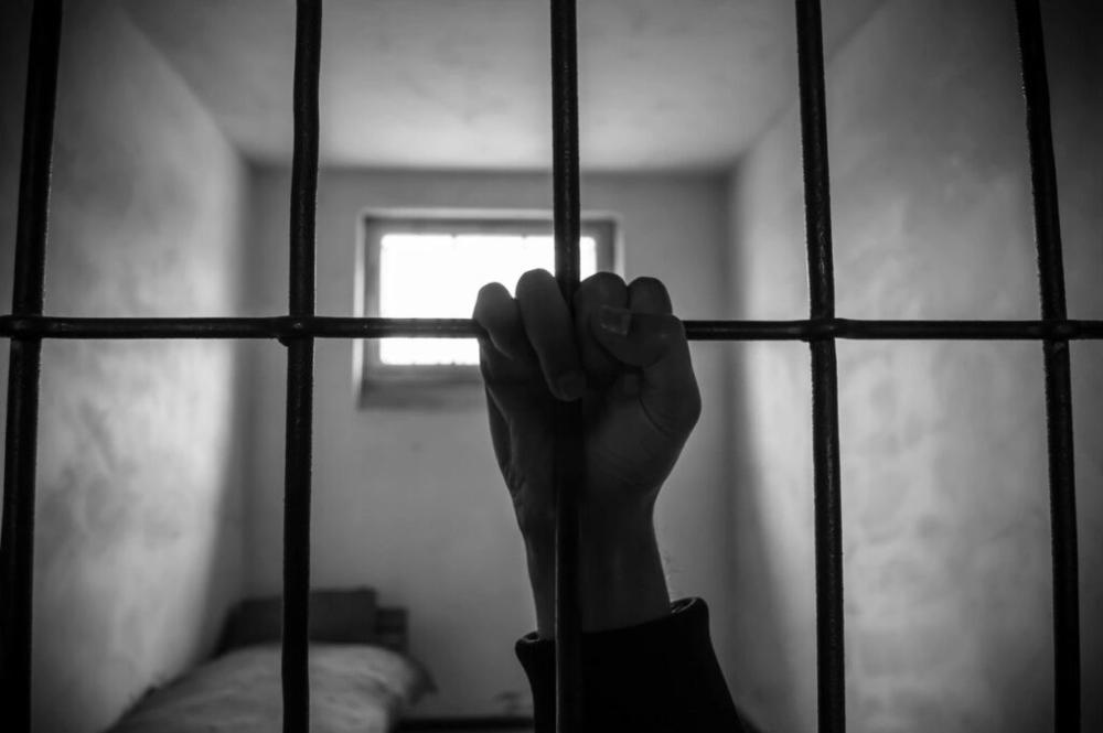 Picture of an inmate's hand holding onto the bar of a jail cell.
