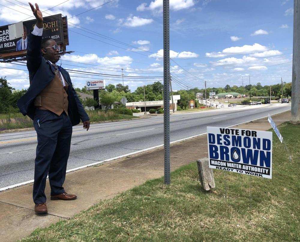 Macon Water Authority incumbent Desmond Brown waves from the sidewalk at Macon Mall where early voting is underway at the Macon-Bibb County Board of Elections. Brown said the mall’s sign prohibition infringes on his ability to campaign.