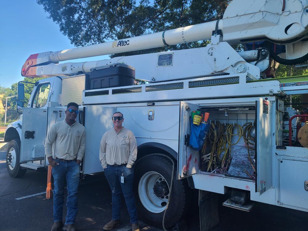 Malachi Eskin and Darci Roles, both Linemen at Georgia Power stand in front of the bucket truck they use to repair electric lines after a storm.