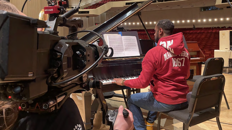 Composer Carlos Simon sitting at a piano.