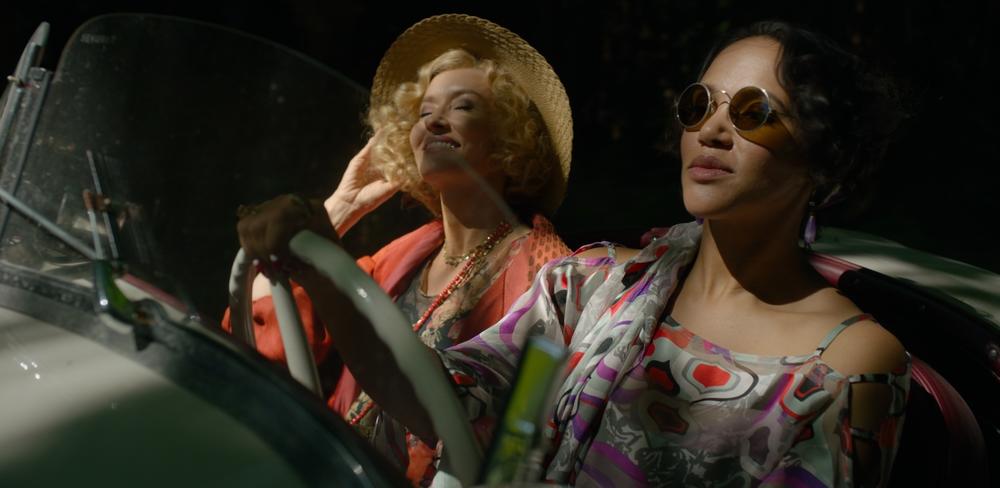 Two women in 30s period dress driving in a convertable.