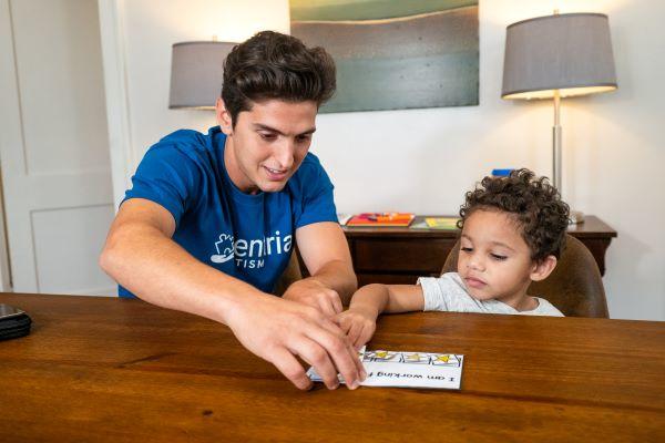 An adult helps a toddler reach something on a table