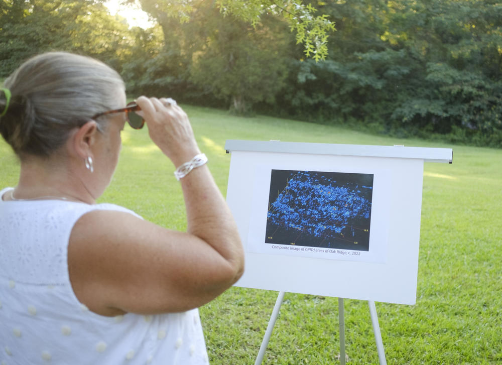 A tour participant looks at a visualization of ground penetrating radar data gathered in the grassy area in the background at Oak Ridge Cemetery. Each blue mark suggests land was used for burial. 