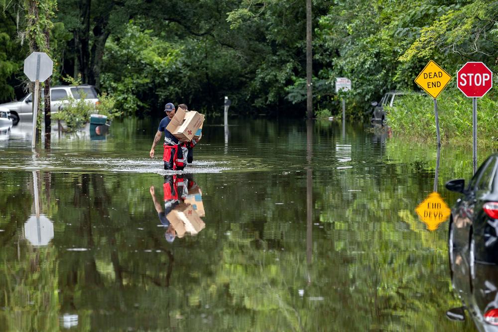 Savannah Fire Advanced Firefighters Andrew Stevenson, front, and Ron Strauss carry food to residents in the Tremont Park neighborhood that where stranded in flooding from Tropical Storm Debby, Tuesday, Aug. 6, 2024, in Savannah, Ga. 