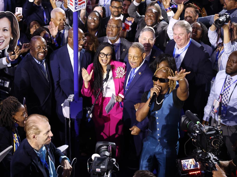 A group of people, including Atlanta Congresswoman Nikema Williams and rapper Lil Jon, are show on the floor of a convention hall.