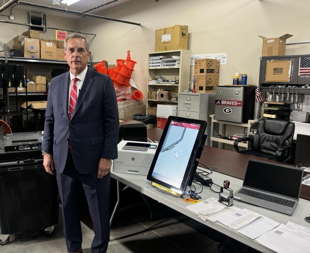 Secretary of State Brad Raffensperger stands with a voting machine