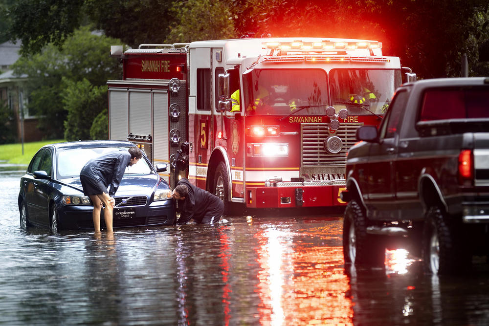 People attach a towline to a stranded vehicle on a flooded street after heavy rain from Tropical Storm Debby, Monday, Aug. 5, 2024, in Savannah, Ga. 