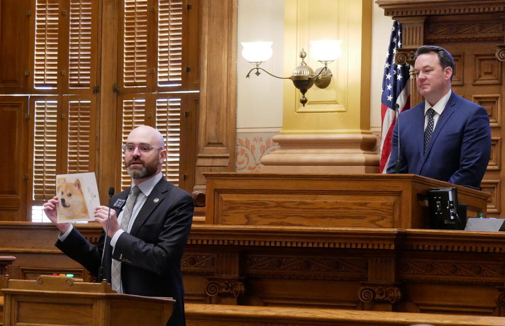  Sen. Josh McLaurin, a Sandy Springs Democrat, holds up a photo of the Doge meme that became popular in 2013 while Lt. Gov. Burt Jones looks on. 