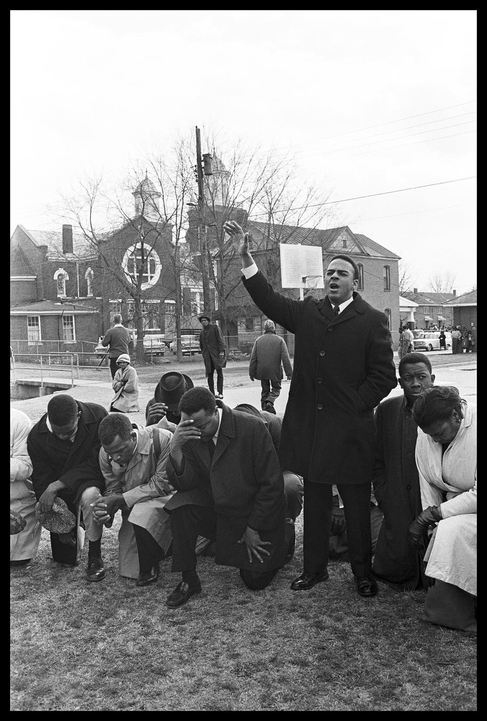 Caption: Andrew Young (right, standing) leads a prayer with Amelia Boynton, the Rev. Hosea Williams, John Lewis, and Bob Mants before the first march to Montgomery on March 7, 1965.  Credit: Spider Martin/Briscoe Center for American History