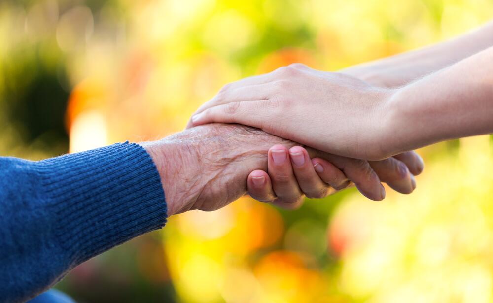 An elderly hand is held by a pair of youthful ones.