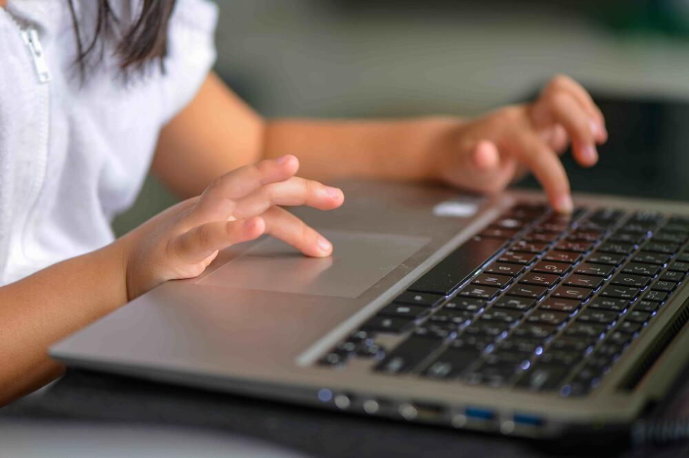 A child's hands type on a laptop