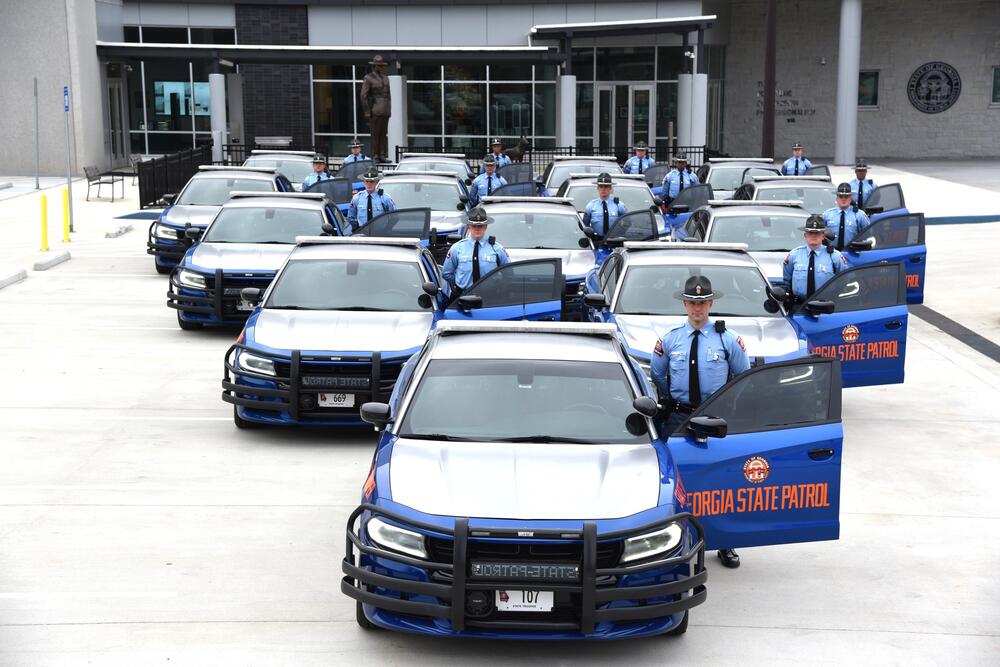 Blue Georgia State patrol cars with officers standing next to them. The cars are arranged in a pyramid formation