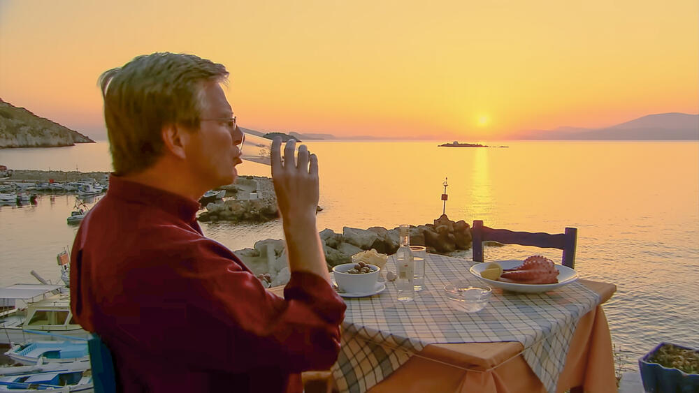 Rick Steves sips a cloudy glass of ouzo at sunset on the Greek isle of Hydra.