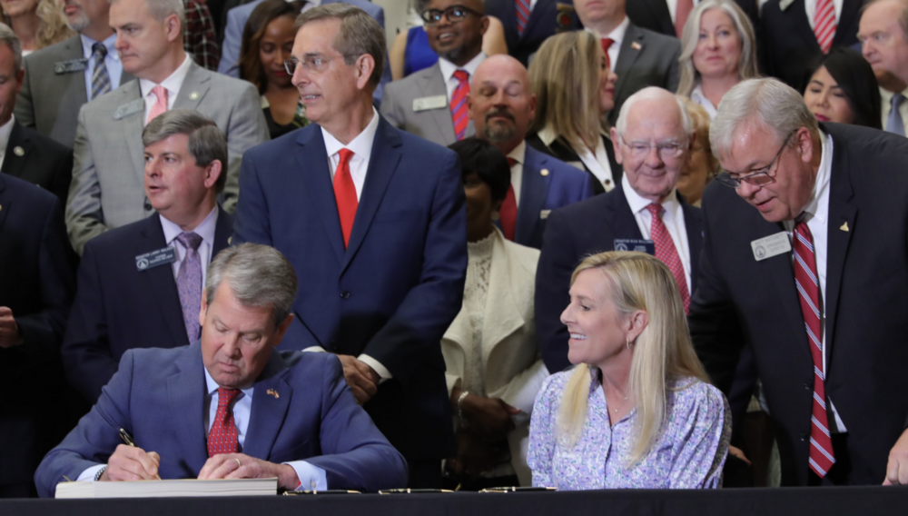 Gov. Brian Kemp (left) signs bills inside the Georgia Capitol on May 8, 2025 as first lady Marty Kemp (right), Secretary of State Brad Raffensperger (center) and lawmakers watch.