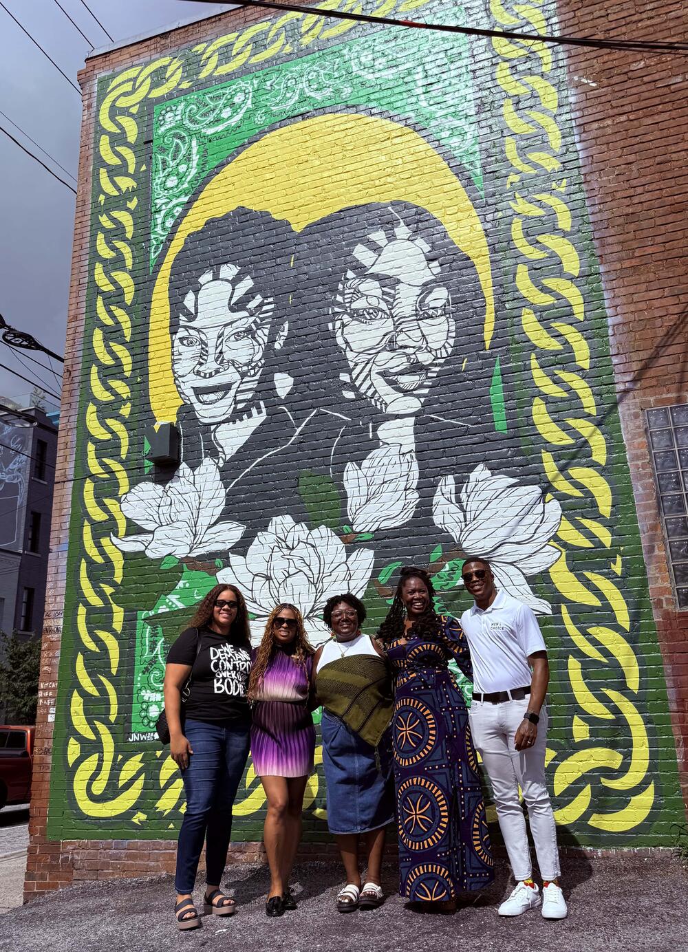 From left to right: Community members Jaylen Black, Alicia Stallworth, Jasmine Nicole Williams, Dr. Karenne Fru, and Davan'te Jennings stand in front of “Born Together” mural in Atlanta Ga. Abisola Dahunsi/GPB News