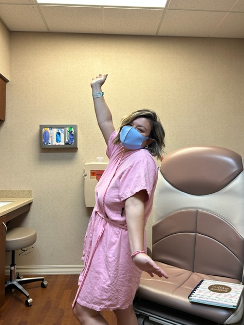 Brittney Powell wears a mask and hospital gown in a hospital room