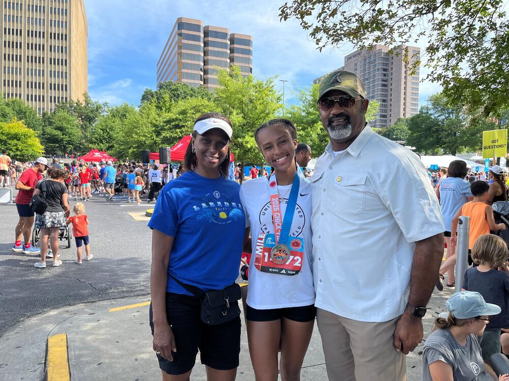 Kaila Alexander and her parents pose and smile. Kaila has a medal and a bib on from the race.