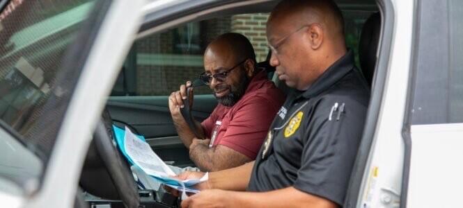 A law officer and another person sit in a car looking at papers