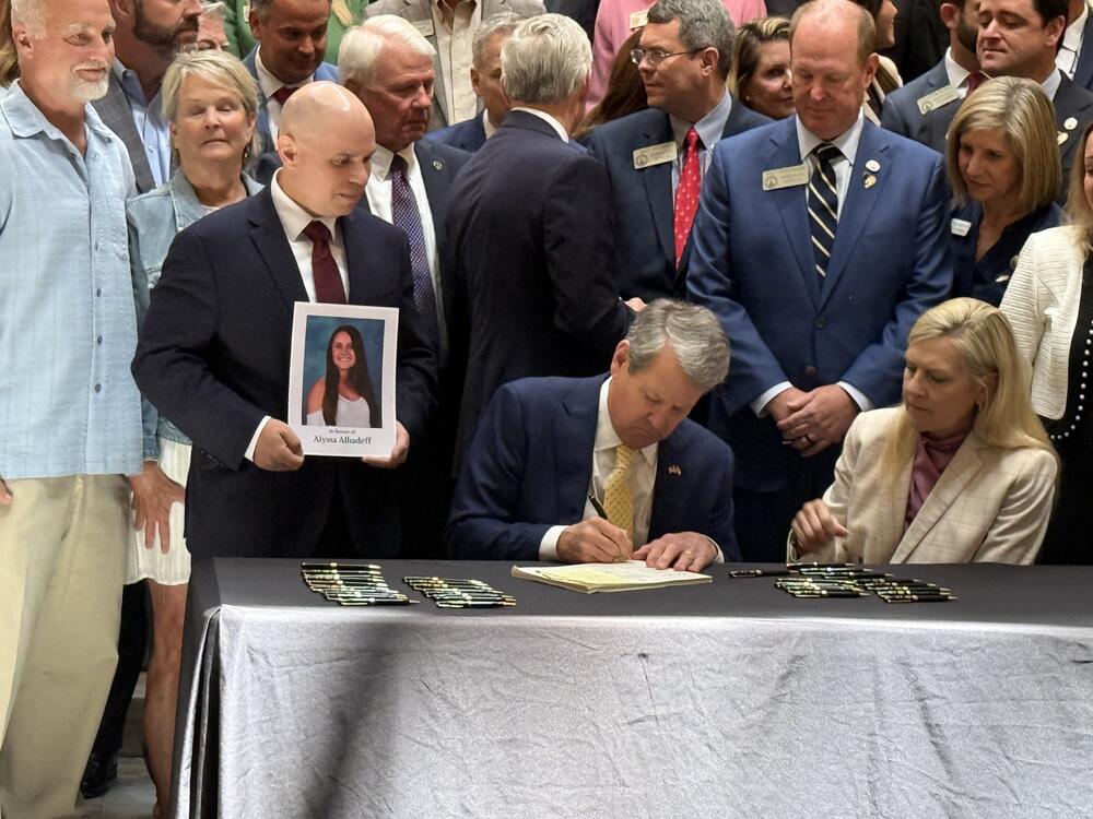 Governor Brian Kemp signs school safety legislation, "Ricky and Alyssa's Law, as Ilan Alhadeff watches holding a photo of his daughter Alyssa. Alyssa was killed in the shootings at Marjory Stoneman Douglas High School in Florida in 2018.  Richard "Ricky" Aspenwall was a math teacher and coach killed at Apalachee High School in Winder, Georgia, in 2024. (April 21, 2025 Georgia Capitol)