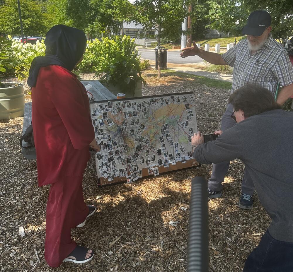 Muzhda Oriakhil (left) and Rusty Pritchard (right) show Chuck a map with birth locations of some of the people helped by Friends of Refugees.